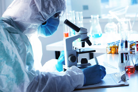 Medical worker in protective gown looking in microscope