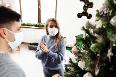 Young couple decorating Christmas tree at home wearing face masksの写真素材