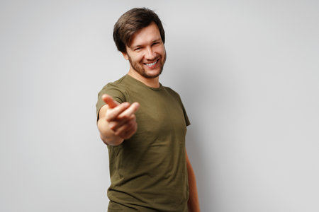 Young man in green t-shirt smiling and gesturing come hereの写真素材