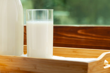 Bottle and glass of milk on wooden table against blurred foliage backgroundの写真素材