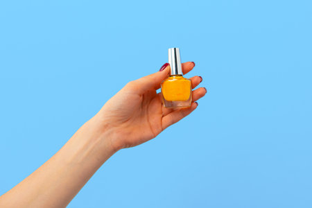 Female hand holding nail polish against blue backgroundの写真素材