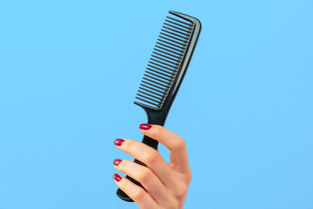 Female hand holding hair comb against blue backgroundの写真素材