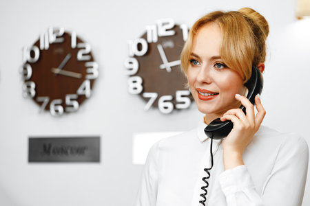 Good-looking friendly woman hotel receptionist talking on the phoneの写真素材