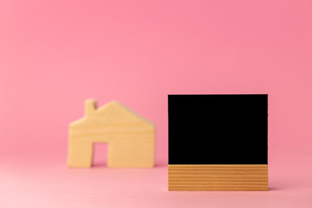 Wooden house miniature and black tag with copy space on pink backgroundの写真素材