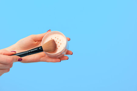 Female hand holding box of loose face powder against blue background