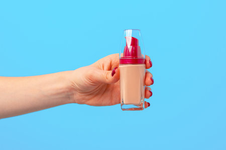 Female hand holding facial foundation against blue backgroundの写真素材