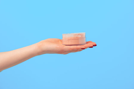 Female hand holding box of loose face powder against blue background
