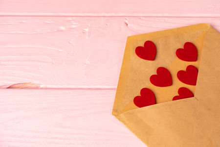 Red heart decoration in envelope on pink wooden table