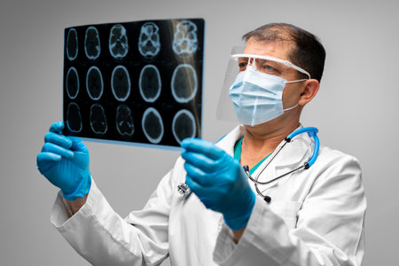 Senior man doctor in mask examines head MRI in hospital