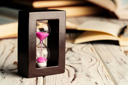 Sandglass on wooden table with opened book close upの写真素材