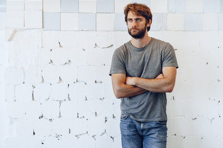Portrait of a young bearded man standing against grunge weathered wall