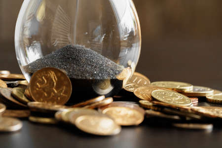 Time is money. Close up of hourglass with money coinsの写真素材