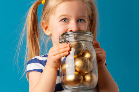 Little cute girl holding glass jar with golden eggs colored for Easterの写真素材