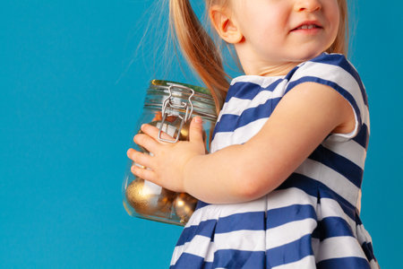Little cute girl holding glass jar with golden eggs colored for Easterの写真素材