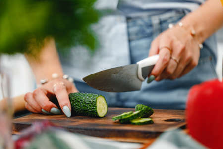 Unrecognizable woman cutting cucumber on wooden board close upの写真素材