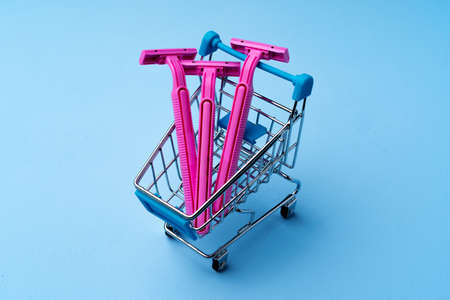Three pink disposable shavers in shopping cart on blue backgroundの写真素材