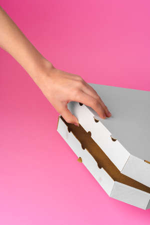 Female hand opening pizza delivery box on pink backgroundの写真素材