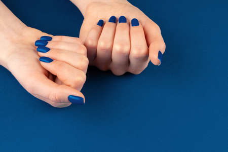 Female hands with manicure of classic blue color on blue backgroundの写真素材