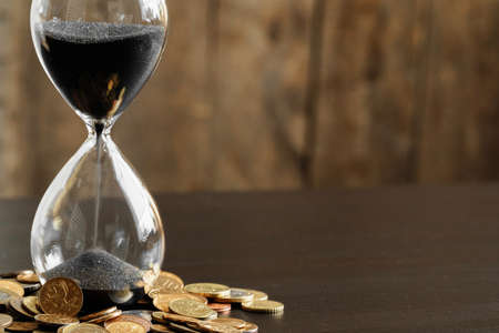 Time is money. Close up of hourglass with money coinsの写真素材