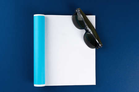 Sunglasses and blank magazine page on classic blue background