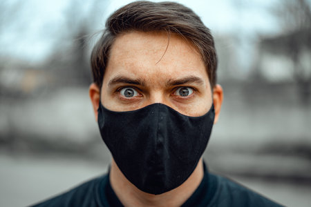 Portrait man in medical mask. Young man stands on light background and looking at camera. COVID-19...