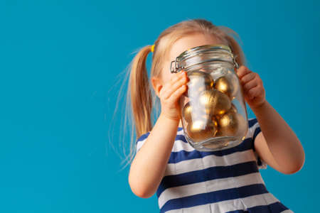Little cute girl holding glass jar with golden eggs colored for Easterの写真素材