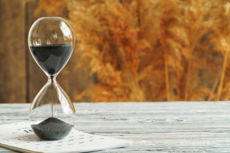 Hourglass with calendar on wooden desk close up