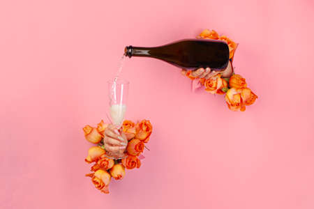 Female hand with manicure pouring champagne into a glass through a hole in a torn paper decorated with rosesの写真素材