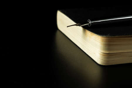 Black notepad with pen on black table close up