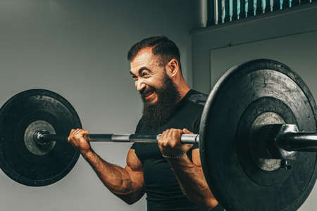 Muscular man in black sportswear lifting barbell in a gymの写真素材