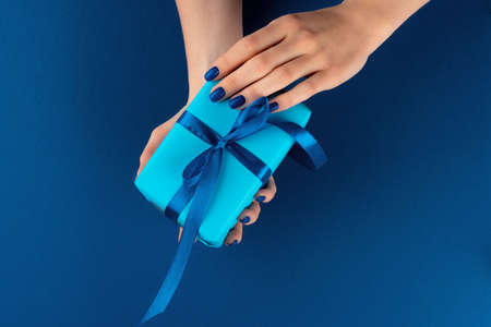 Woman holding gift box with ribbon against classic blue background