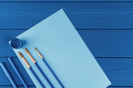 Blue paint brushes on classic blue background, view from above