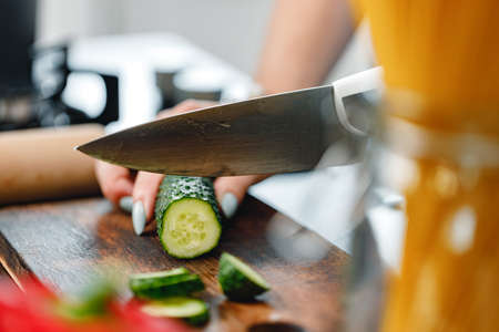 Unrecognizable woman cutting cucumber on wooden board close upの写真素材