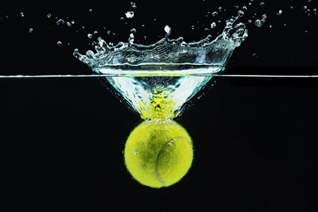 Tennis ball falling in water with a splash against dark backgroundの写真素材