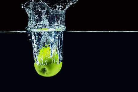 Green apple falling in water with a splash against dark backgroundの写真素材