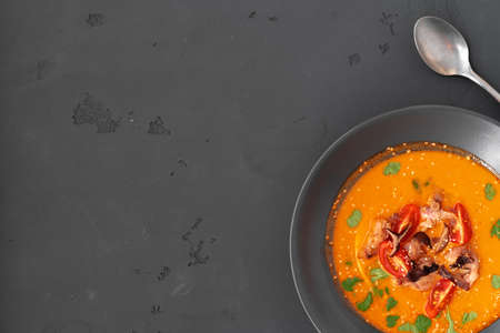 Tom yam Thai soup in black bowl served on gray background