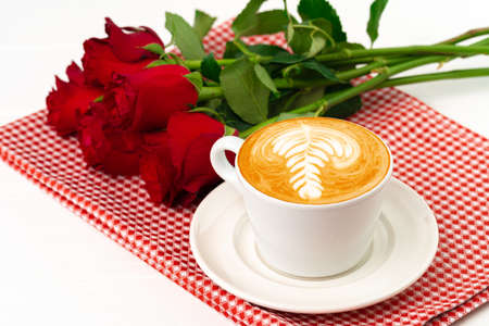 Cup of cappucino with art and bouquet of roses on wooden tableの写真素材