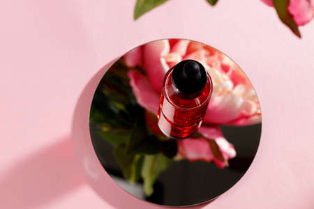 Glass bottle with oil on round mirror on pink backgroundの写真素材