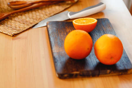 Fresh oranges on wooden cutting board and knife on kitchen tableの写真素材