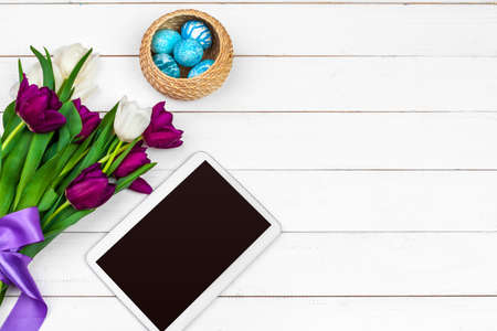 tablet screen for message and colorful tulips and easter eggs on wooden backgroundの写真素材