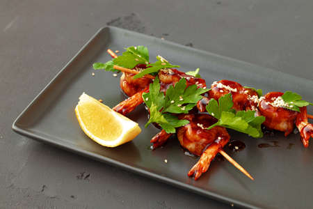 Grilled shrimps on skewers with teriyaki sauce on black ceramic plate