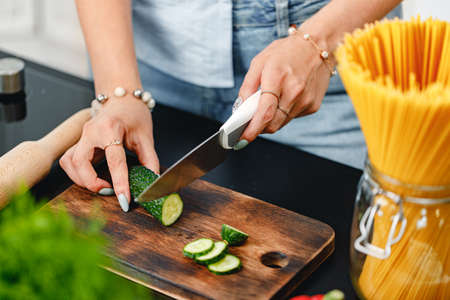 Unrecognizable woman cutting cucumber on wooden board close upの写真素材