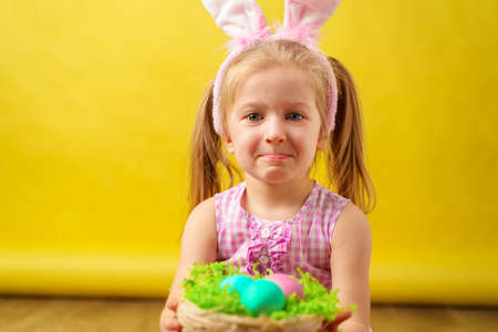 Toddler blonde happy girl with bunny ears and basket of eggs for Easterの写真素材
