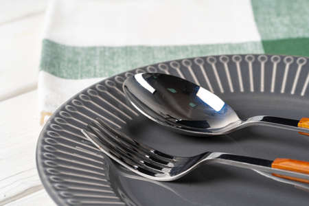Glossy grey ceramic plate with cutlery on wooden table