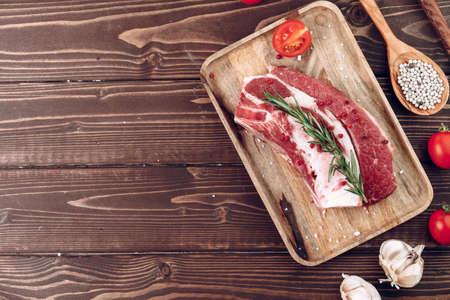 Raw beef steak with rosemary and spices on wooden board