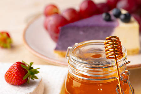 Glass honey jar on background of fruits and sweetsの写真素材