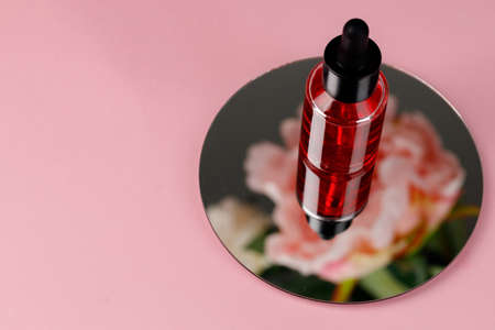 Glass bottle with oil on round mirror on pink background