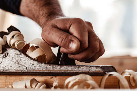 Carpenters hands planing a plank of wood with a hand plane