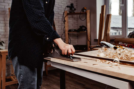 Carpenters hands planing a plank of wood with a hand plane