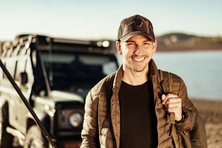 Young fisherman standing near his car and holding fishing equipmentの写真素材